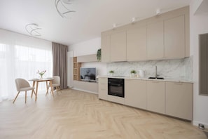 Eine moderne Küche mit Einbauofen, ein Essbereich mit Tisch und Stühlen sowie ein Fernseher.