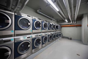 A row of industrial-style washing machines in a facility with visible ductwork and a clean, utilitarian design. - Functional Studio Close to the Metro in Warsaw by Noclegi Renters (Warszawa)