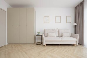 A minimalist living room with a light-colored sofa, a small side table with a plant, and a large wardrobe. There are three framed pictures on the wall. - Functional Studio Close to the Metro in Warsaw by Noclegi Renters (Warszawa)