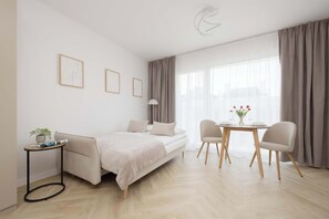 A modern, well-lit room with a bed, a small table with a plant, and a dining area with chairs and a table set for two. - Functional Studio Close to the Metro in Warsaw by Noclegi Renters (Warszawa)