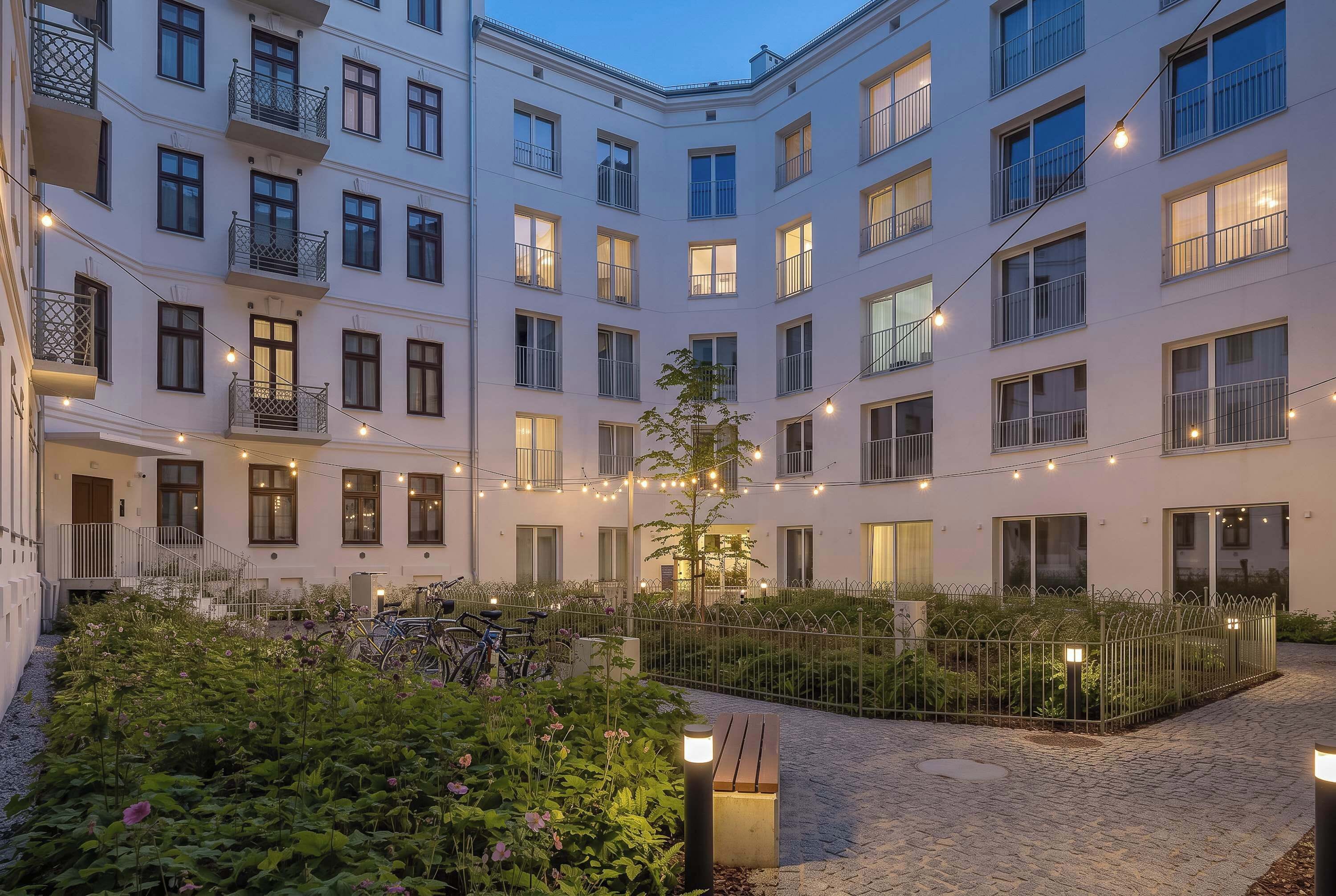 Un edificio residencial de varios pisos con balcones, un patio con plantas y bicicletas.