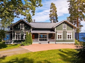 Ein zweistöckiges Haus mit Veranda, großen Fenstern und Blick auf das Wasser.