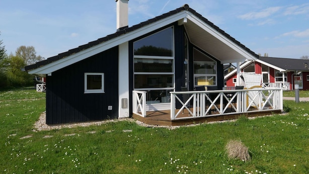 Ein modernes Haus mit einem großen Glasfenster, einer Terrasse mit weißen Geländern und einem Schornstein.