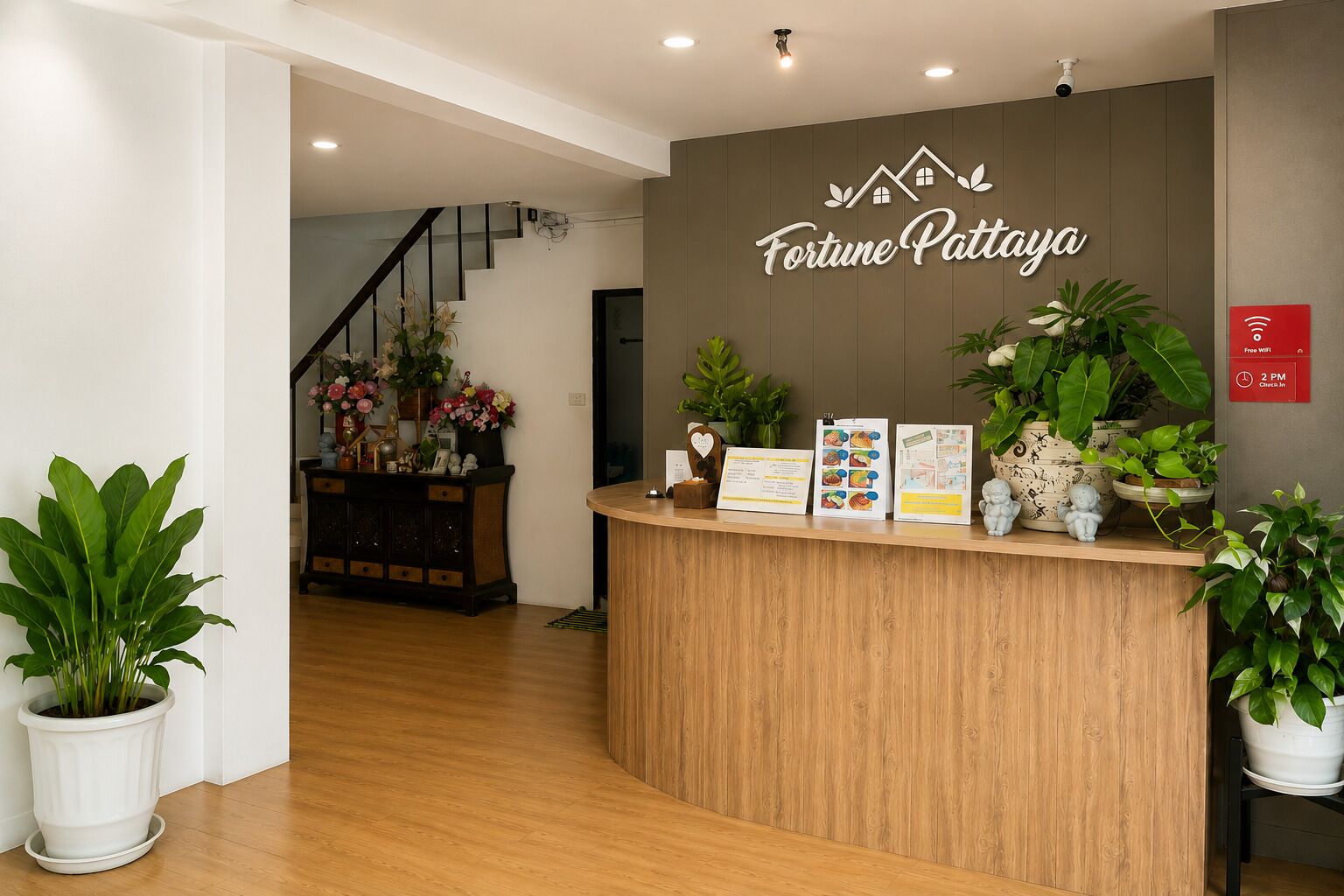 Een receptiebalie met een bordje waarop 'Fortune Pattaya' staat, een trap op de achtergrond en potplanten aan weerszijden.