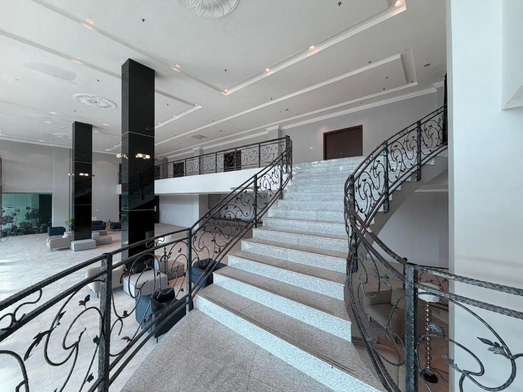 Un hall d’entrée spacieux avec un grand escalier, un comptoir de réception et un espace détente doté de mobilier moderne.