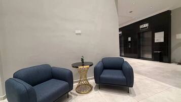 A modern lobby with two sofas and a small round table, a sign indicating 'LIF 1', and a tiled floor.