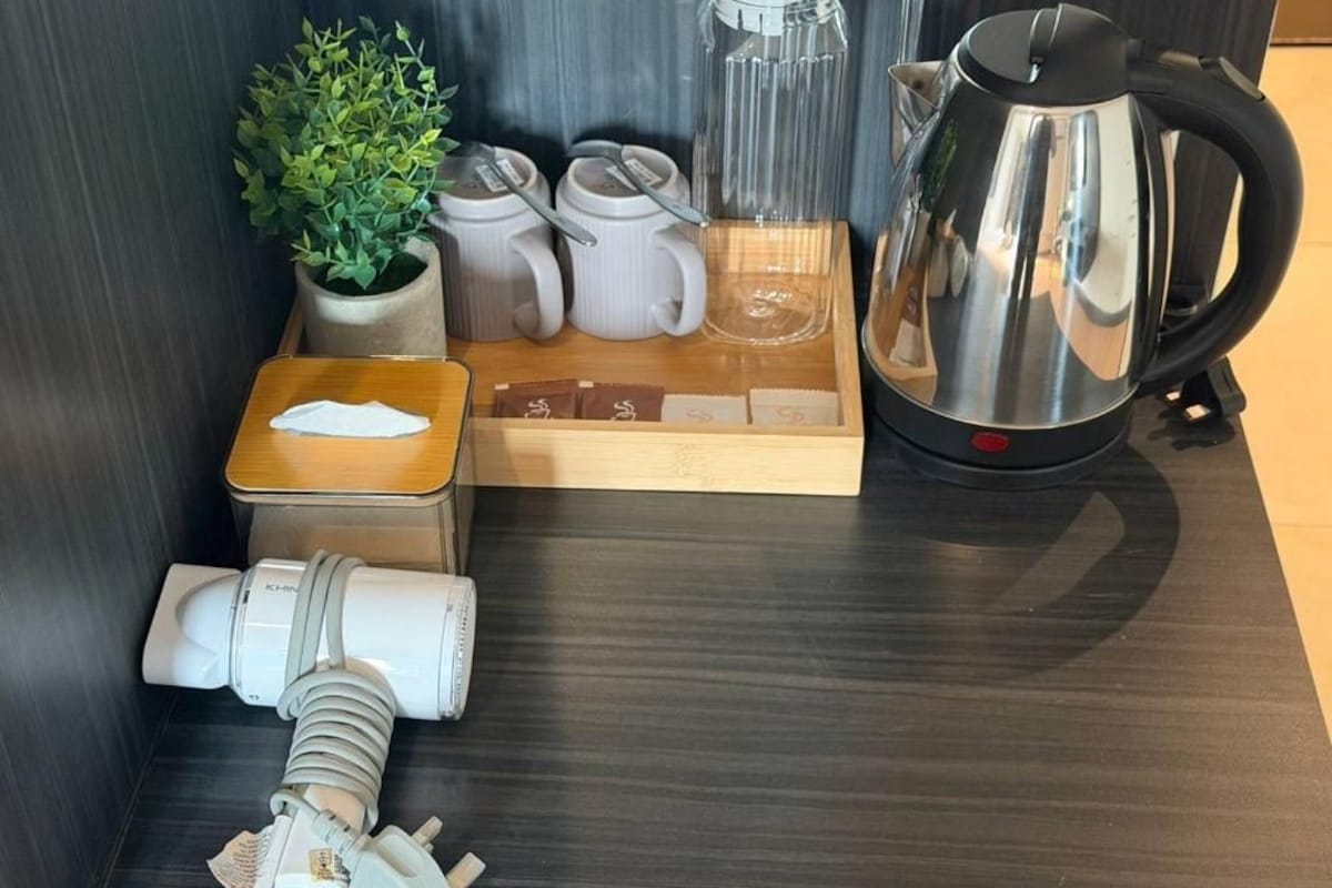 Cozinha compacta com cafeteira, chaleira, uma planta e um tabuleiro com saquinhos de chá.