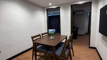 Quarto com uma mesa de jantar de madeira e cadeiras, uma pequena planta e uma porta que dá para outro cômodo.