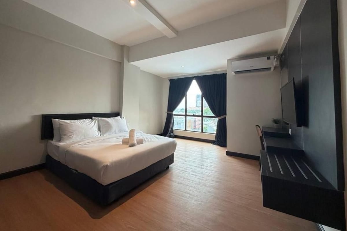 Quarto de hotel com cama, televisão e janela com cortinas.