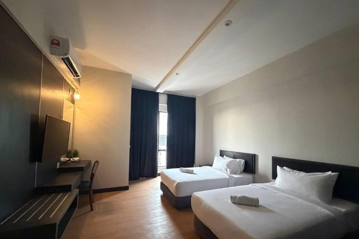 Quarto de hotel com duas camas, uma escrivaninha, uma cadeira e uma televisão.