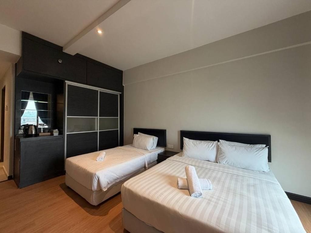 A hotel room with two beds, a dark-colored wardrobe, and a small kitchenette.