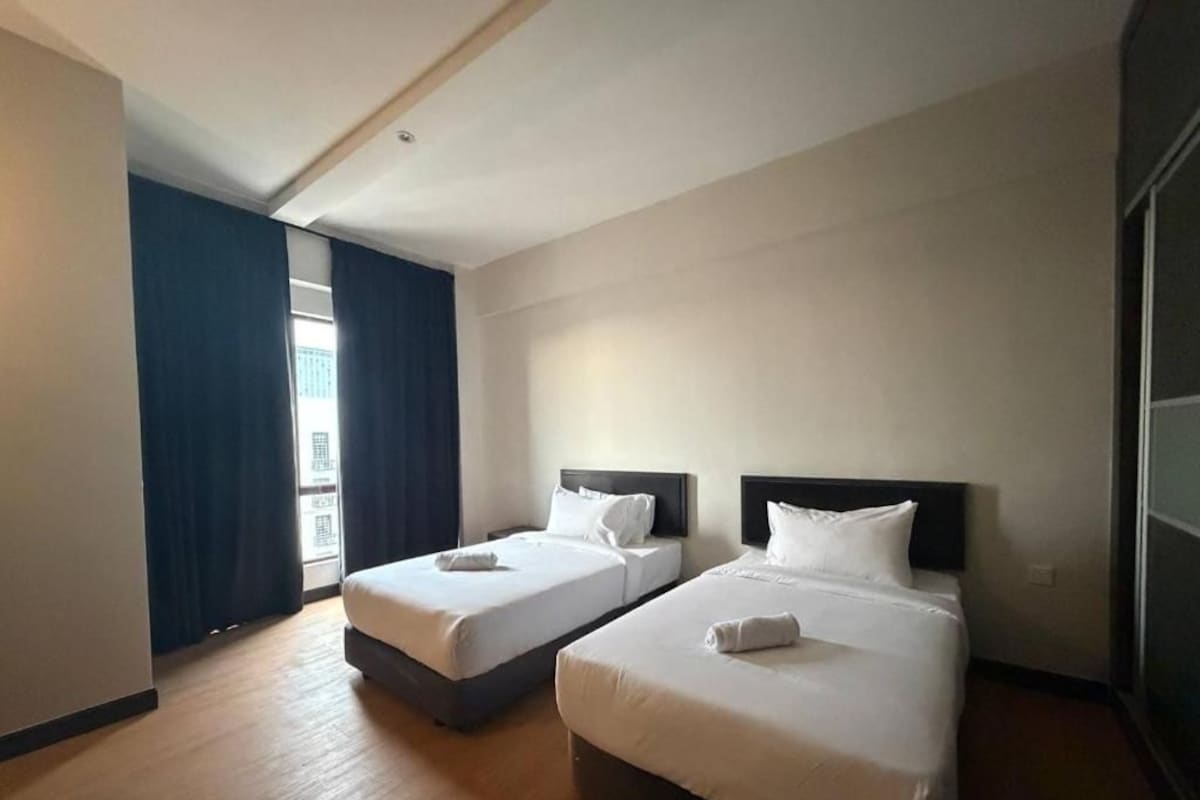 Ett hotellrum med två sängar, ett stort fönster med gardiner och utsikt över omgivningen.