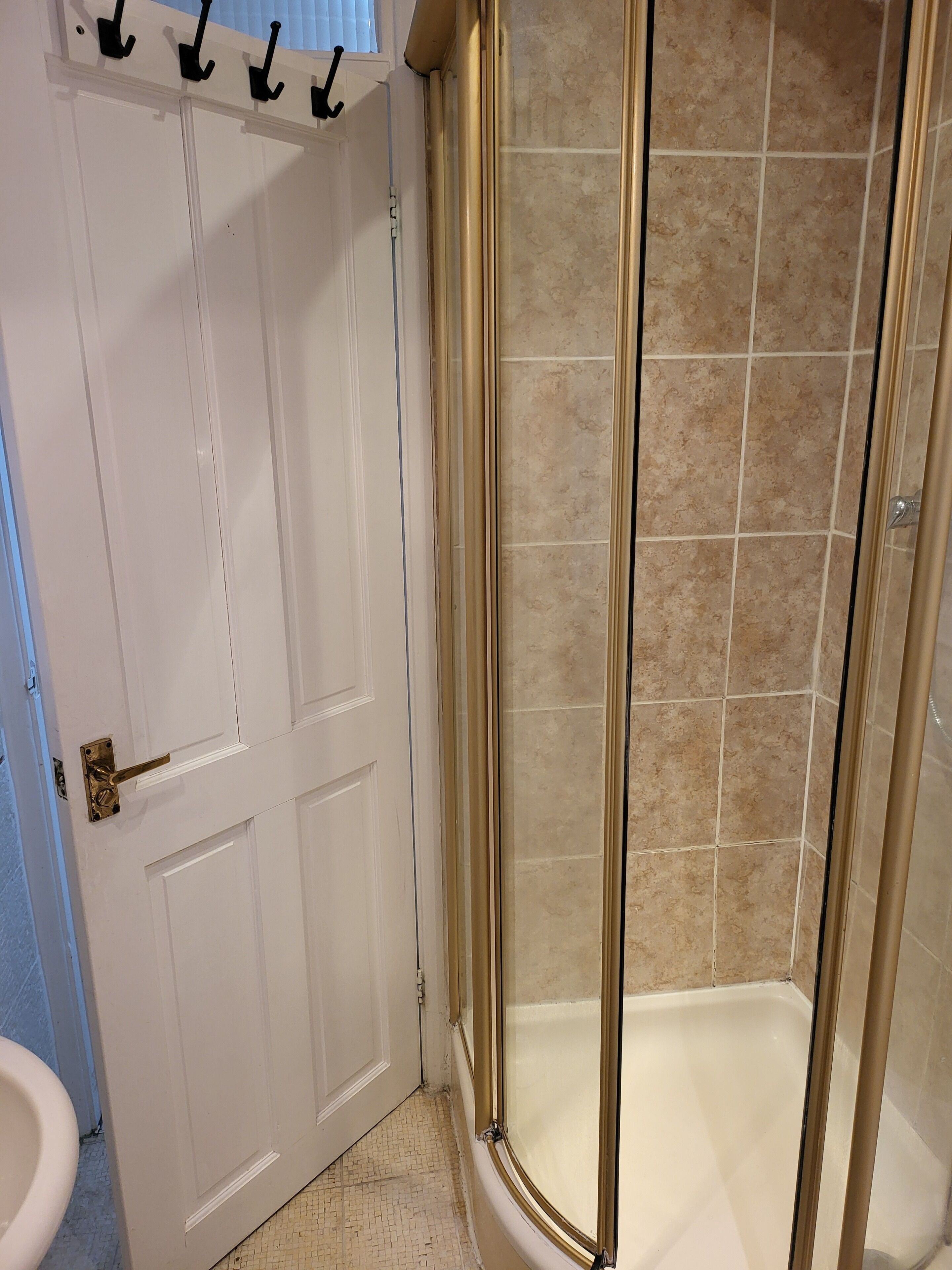 A bathroom with a white door, a shower with a glass door, and a tiled floor.