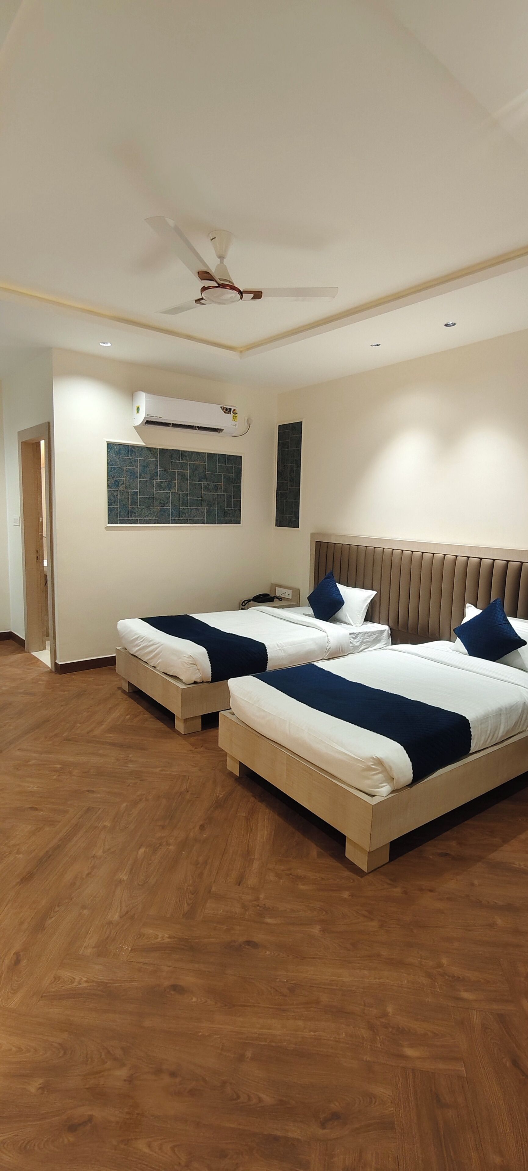 A hotel room with two beds, a ceiling fan, an air conditioning unit, and a tiled wall.