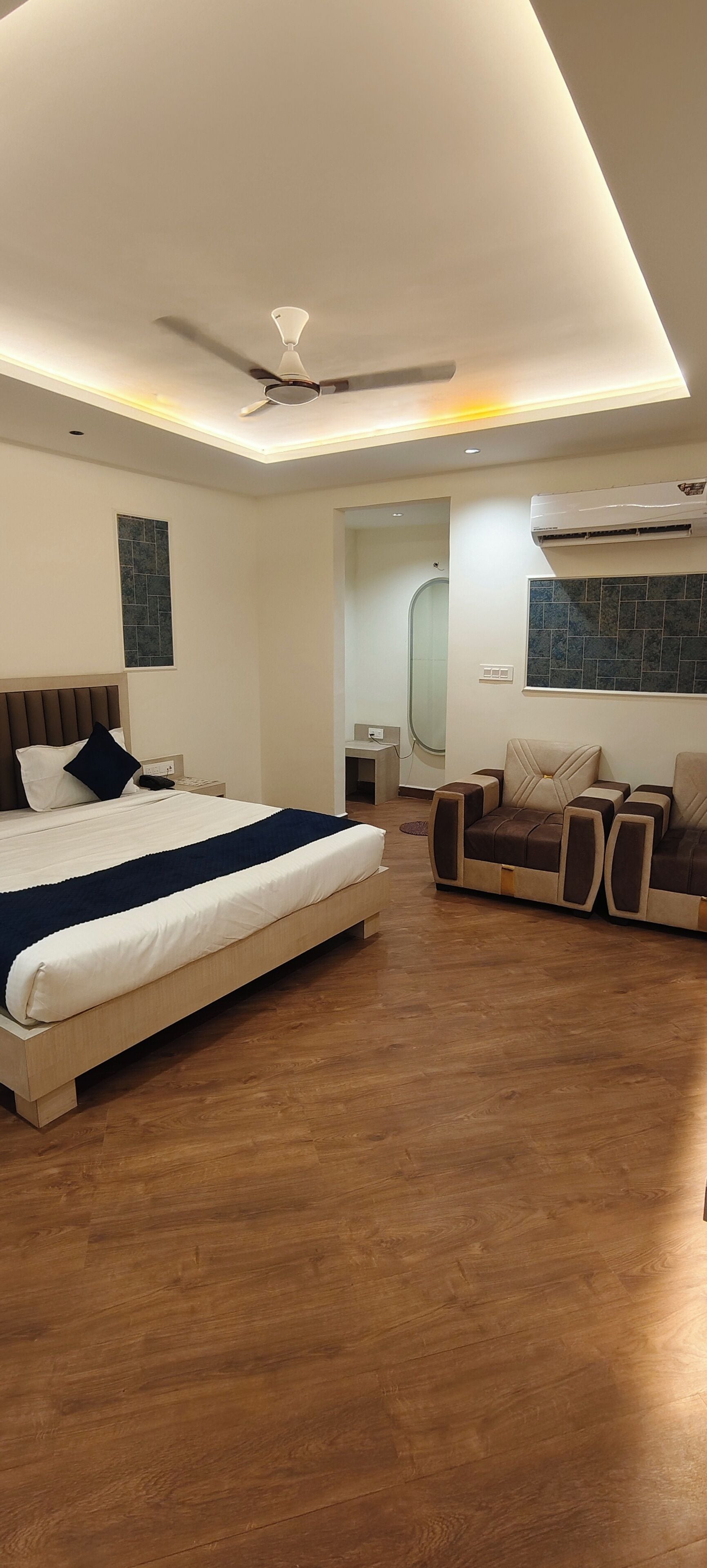 Un dormitorio moderno con cama, sofá, ventilador de techo y aire acondicionado.