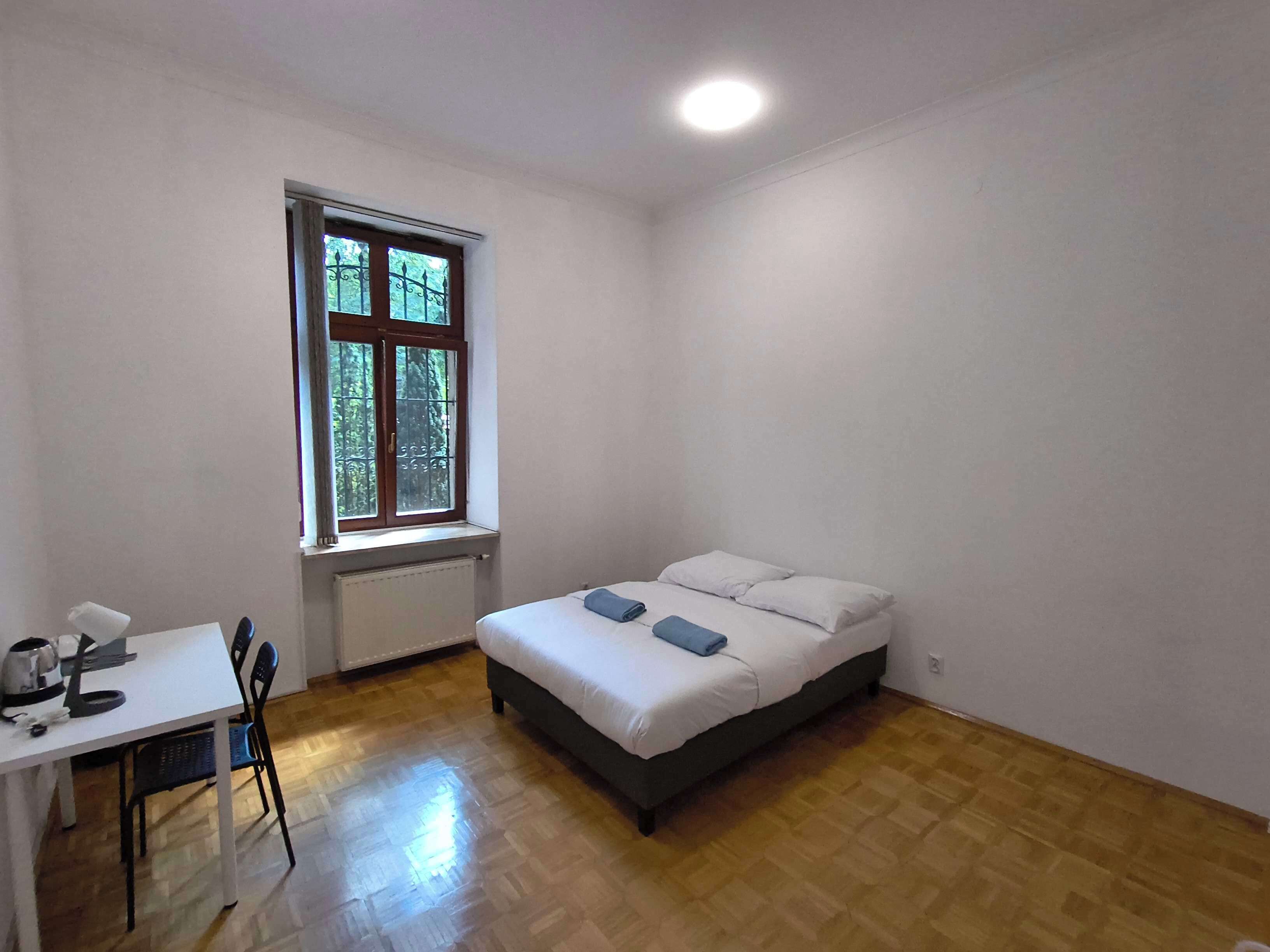 Une pièce avec un lit, une table et des chaises, une fenêtre et un radiateur.