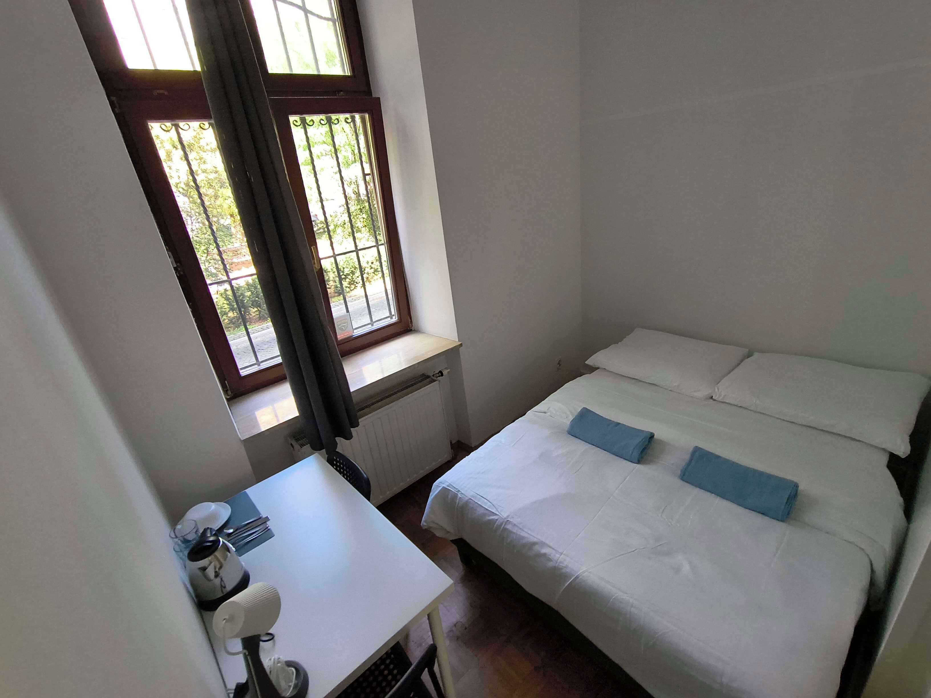 A small, single-bed room with a window, a radiator, a desk with a chair, and a telephone.