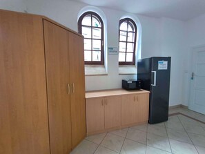A kitchen with wooden cabinets, a black refrigerator, and two arched windows.