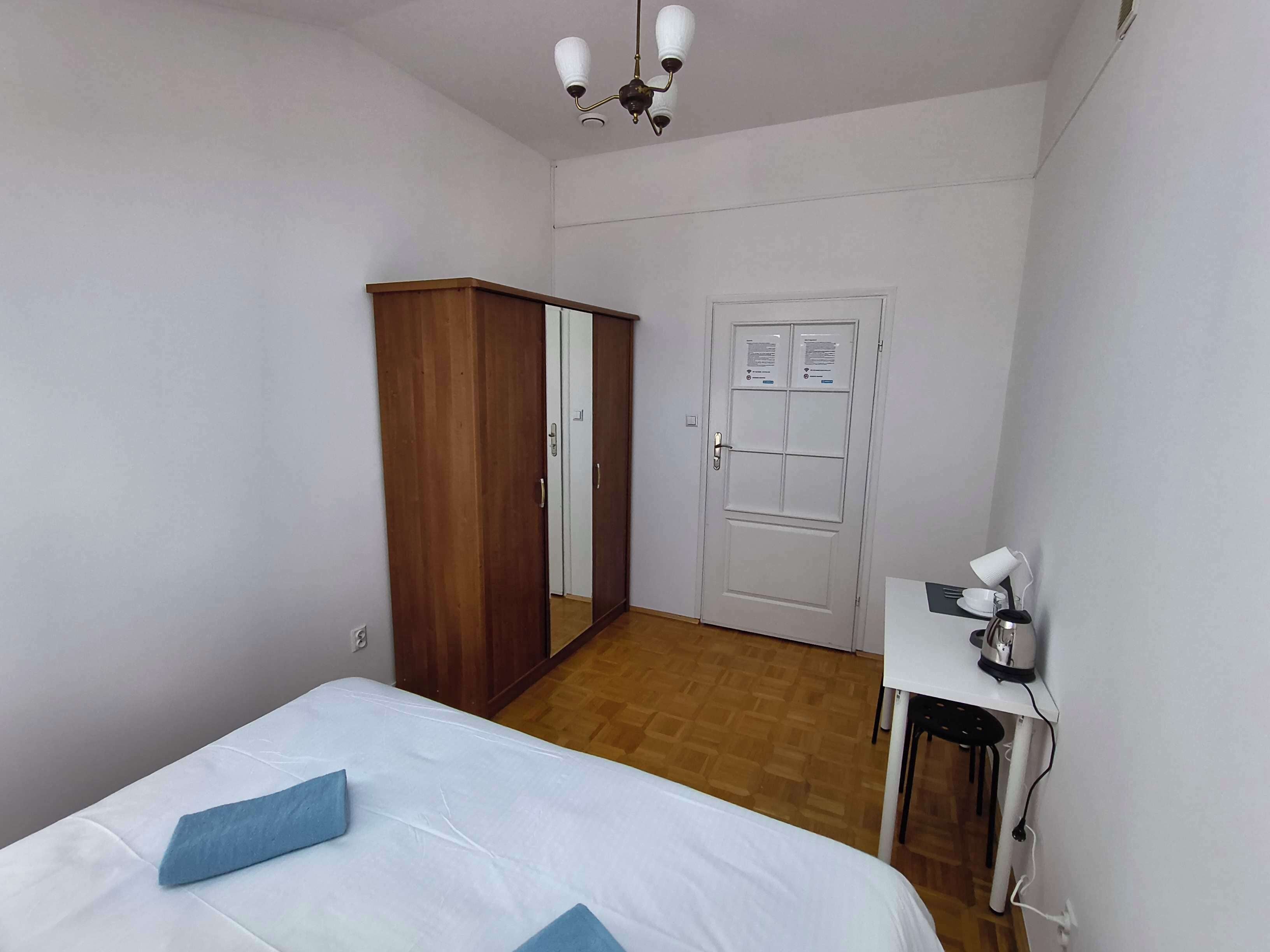 Une chambre à coucher comprenant un lit, une armoire, une porte avec un avis affiché, et une petite table avec une bouilloire.