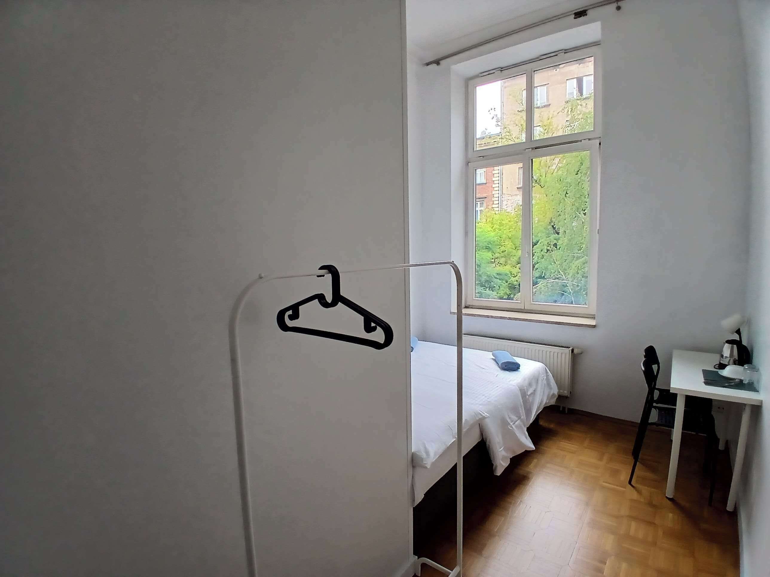 Ein schlichter, einfach eingerichteter Raum mit einem Einzelbett, einem Schreibtisch und einem Fenster mit Blick auf Grünflächen.