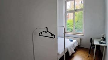 Ein schlichter, einfach eingerichteter Raum mit einem Einzelbett, einem Schreibtisch und einem Fenster mit Blick auf Grünflächen.