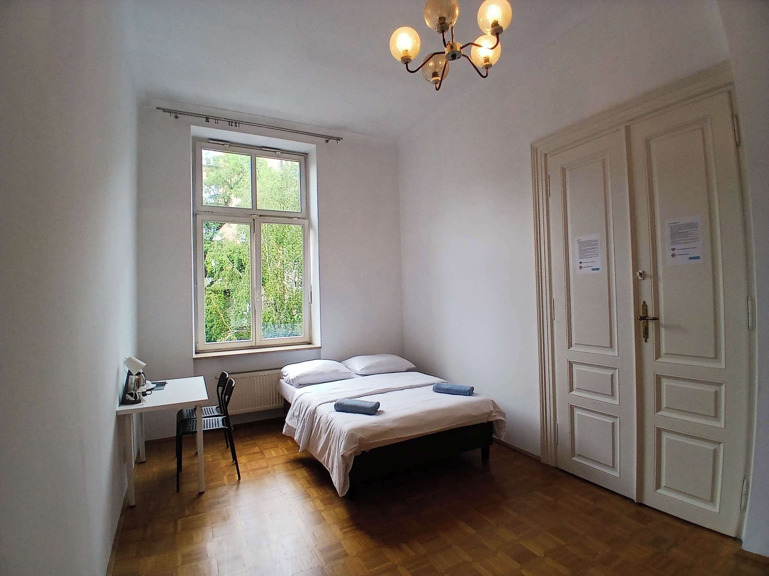 A bedroom with a bed, a desk, a chair, a window, and a door.