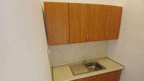 A compact kitchen with a single sink, wooden cabinets, and a tiled backsplash. - Fantastic Inn Kraków - B7 (Kraków)