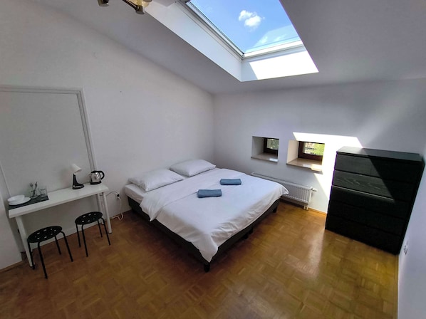 Une chambre avec un puits de lumière, un lit, un bureau avec des chaises et une commode.