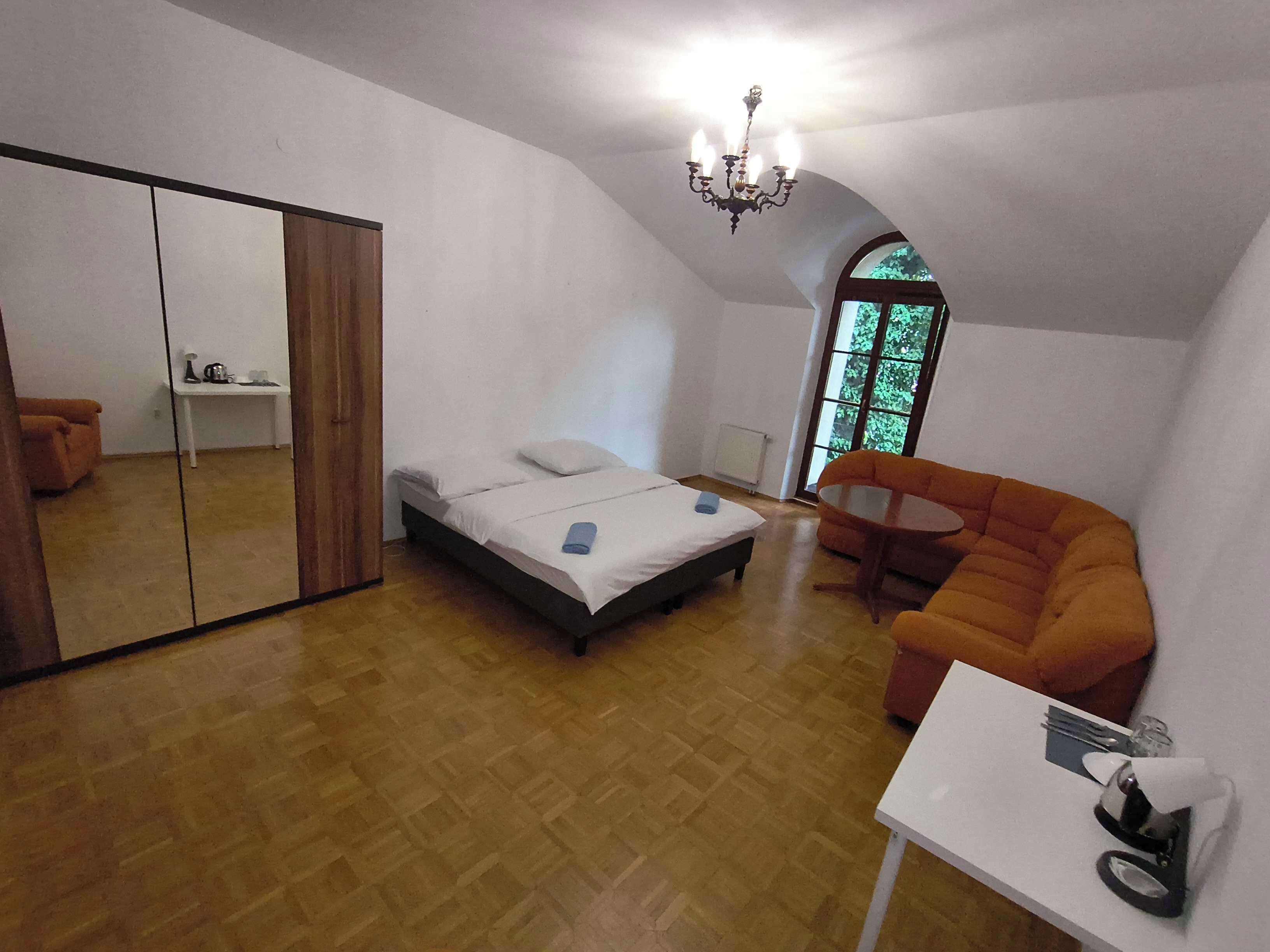 A bedroom with a bed, a mirror, a window, and a small table with a chair.