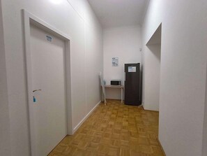 A hallway with a door on the left, a small table with a microwave and a water bottle, and a refrigerator on the right. - Fantastic Inn Kraków - B7 (Kraków)