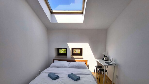 A compact bedroom with a skylight, a bed with white linens, a desk with a chair, and a small TV on the wall. - Fantastic Inn Kraków - B7 (Kraków)