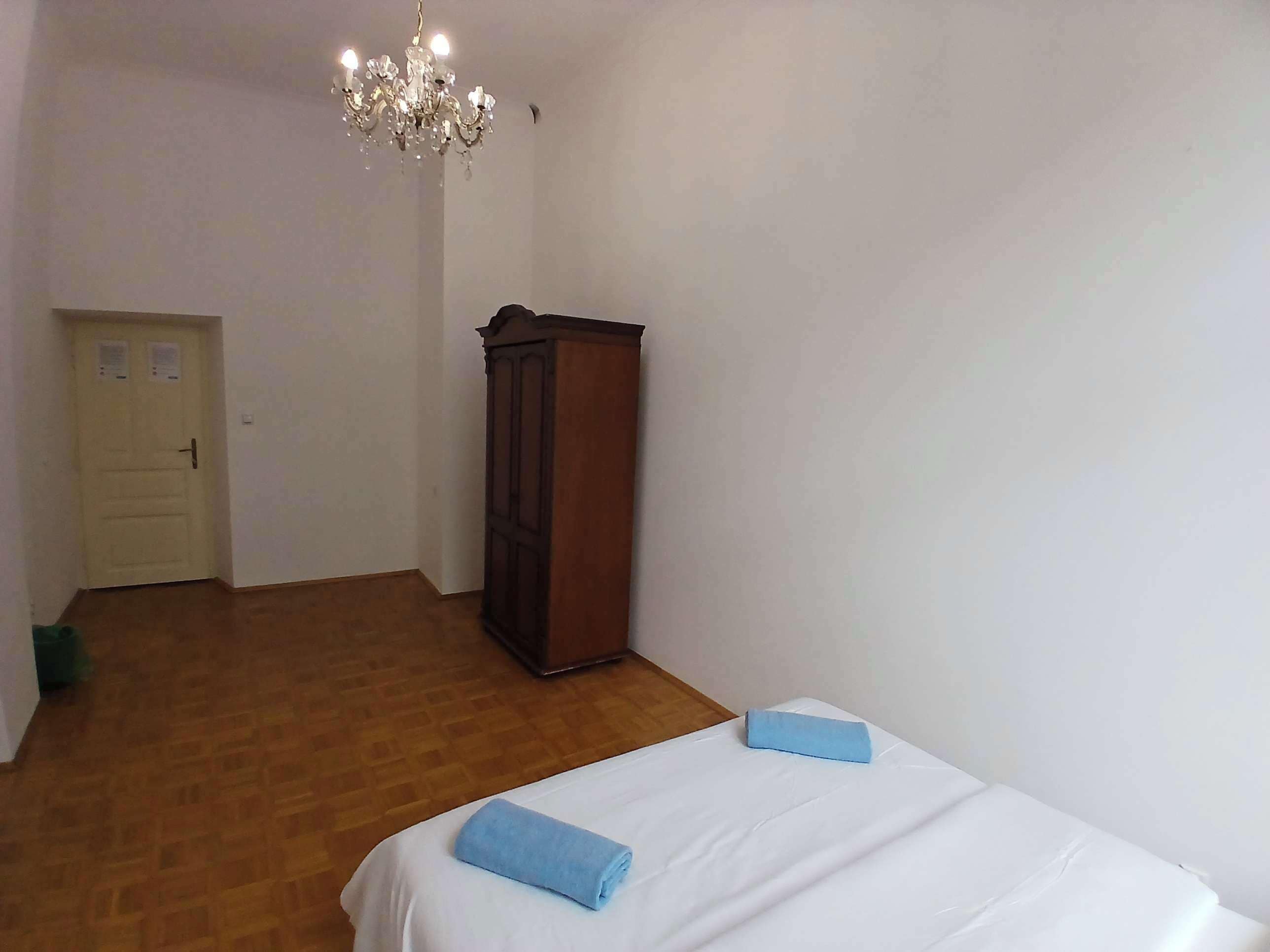 A room with a bed, a wooden wardrobe, a door, and a chandelier.
