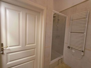 Une salle de bain avec une porte blanche, une douche avec une porte en verre et un porte-serviettes blanc.