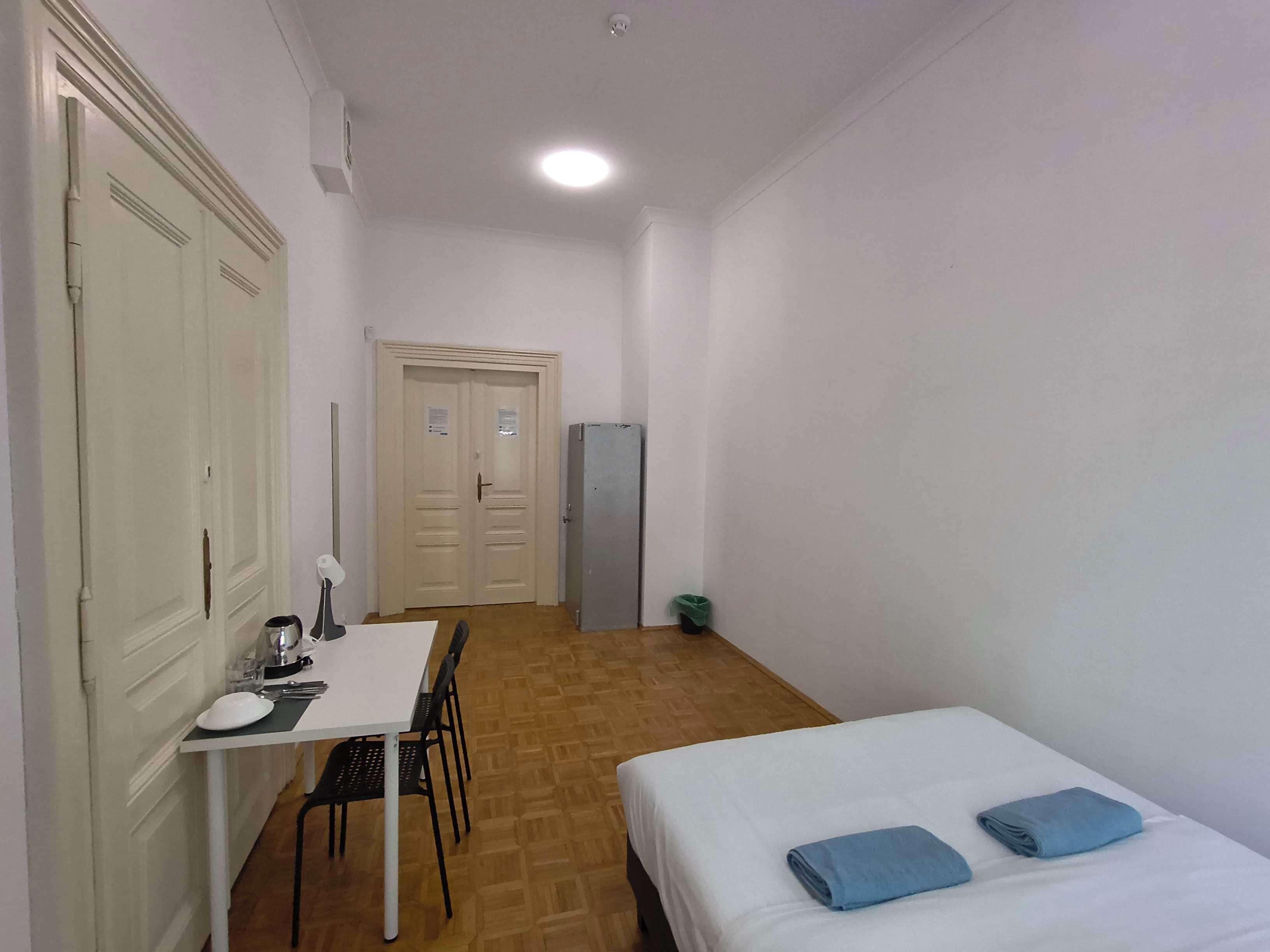 Una habitación con cama, una mesa y sillas, un refrigerador y una puerta.