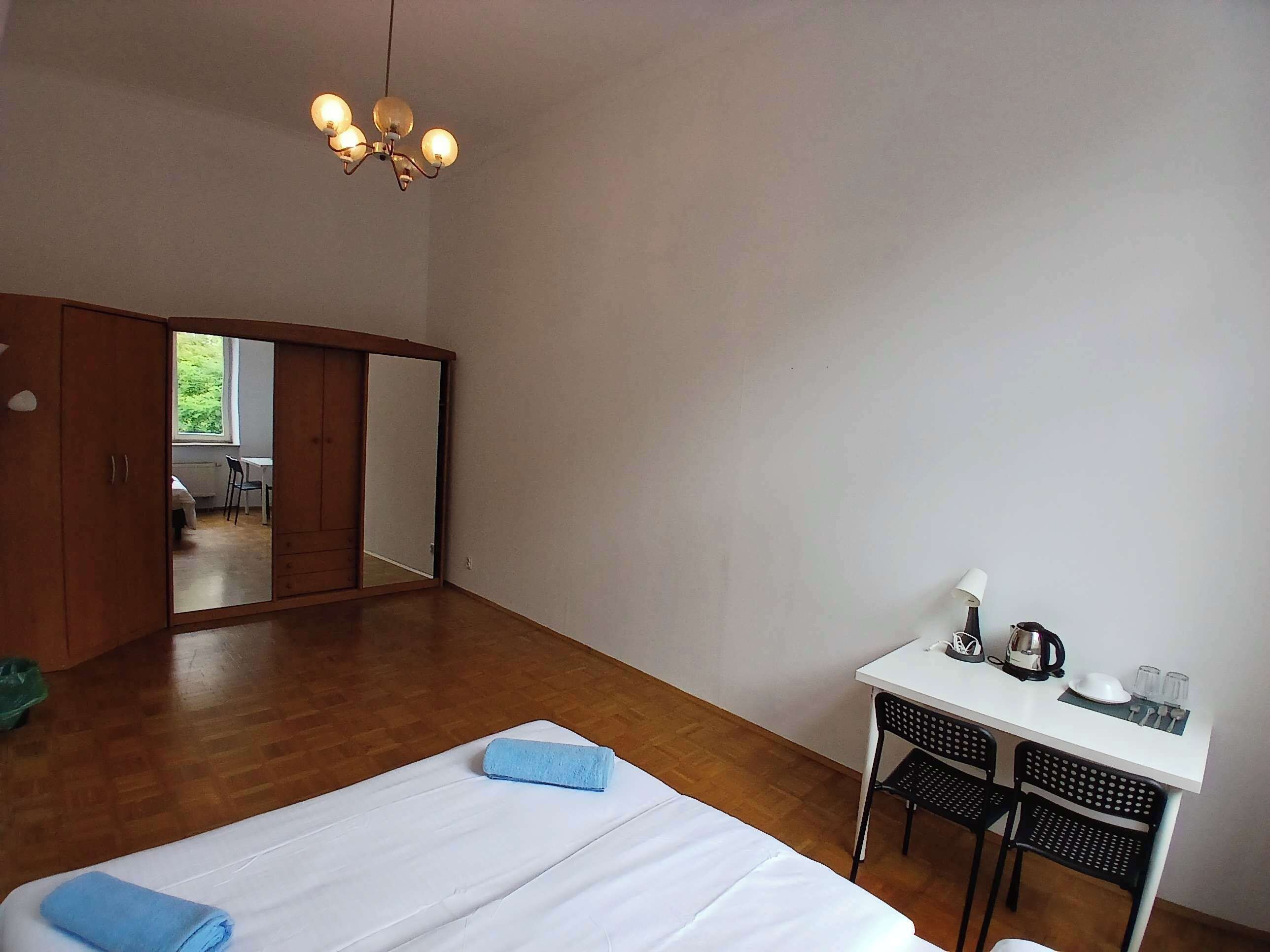 A bedroom with a bed, a desk, and a chair. There is a wardrobe and a mirror.