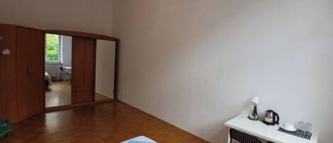 A bedroom with a bed, a desk, and a chair. There is a wardrobe and a mirror.