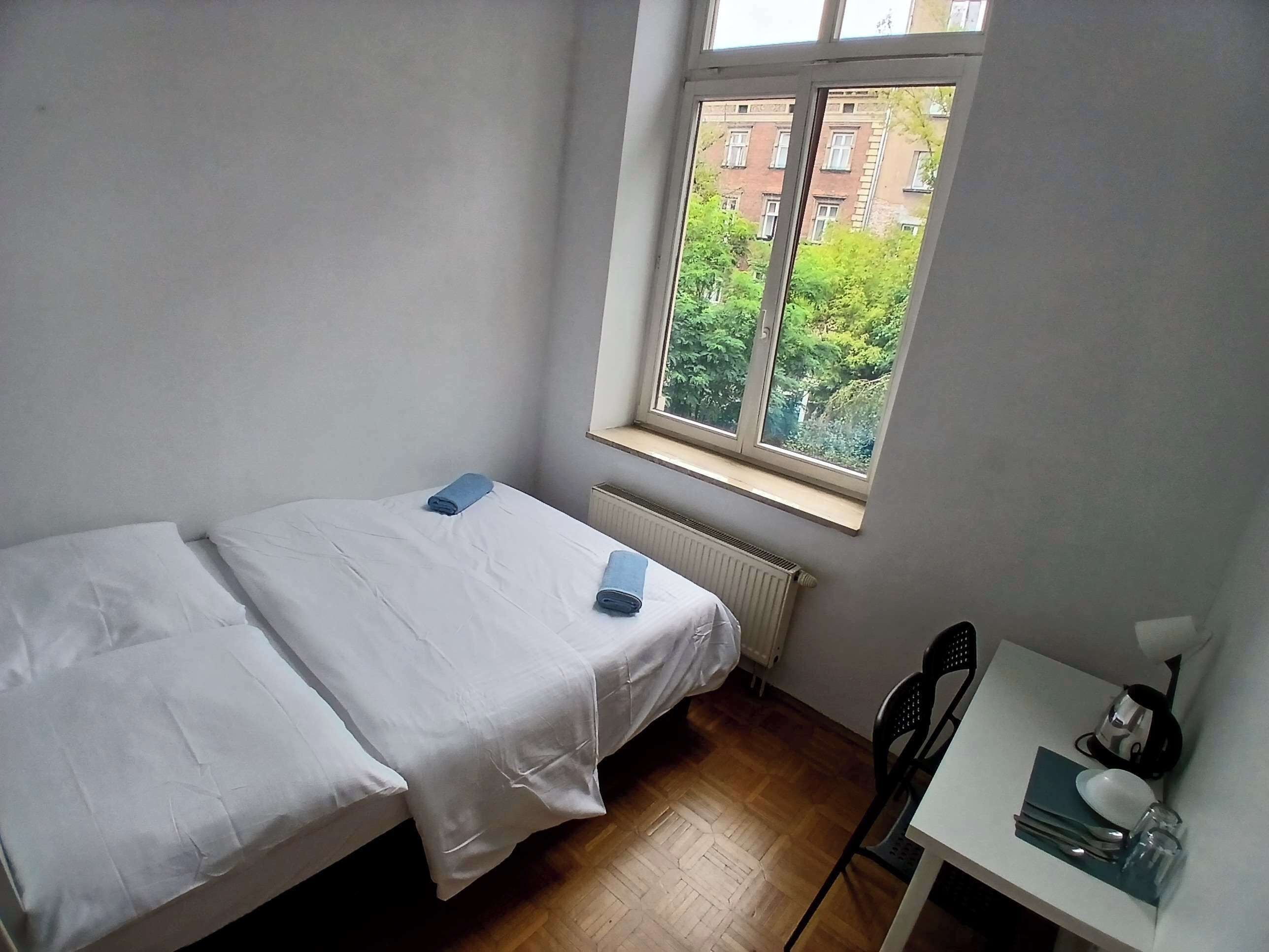 A small, single-bed room with a window overlooking a building and greenery.