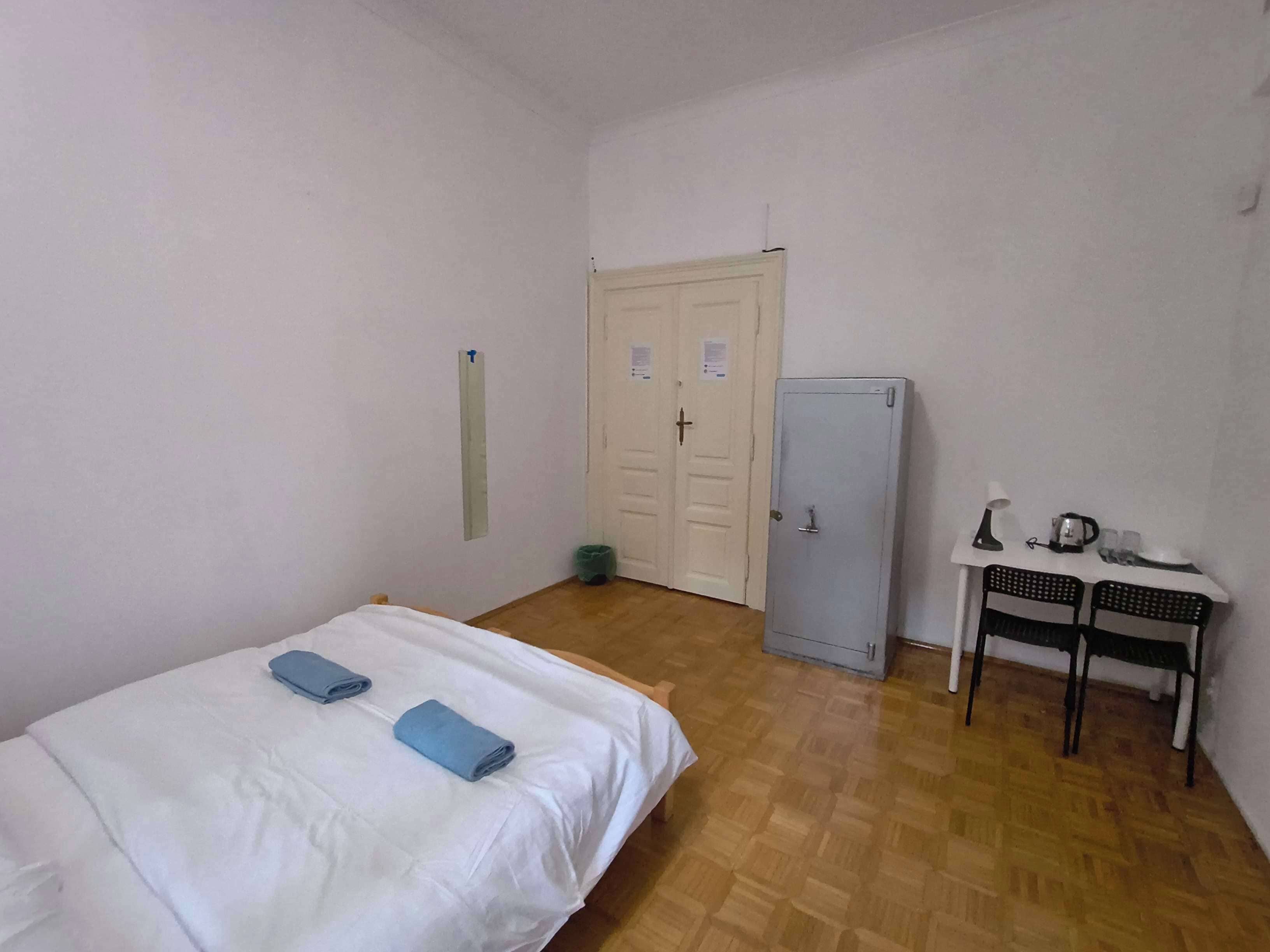 Une chambre avec un lit, une petite table sur laquelle se trouvent une bouilloire, des tasses et une lampe, ainsi qu’une porte sur laquelle est affiché un avis.