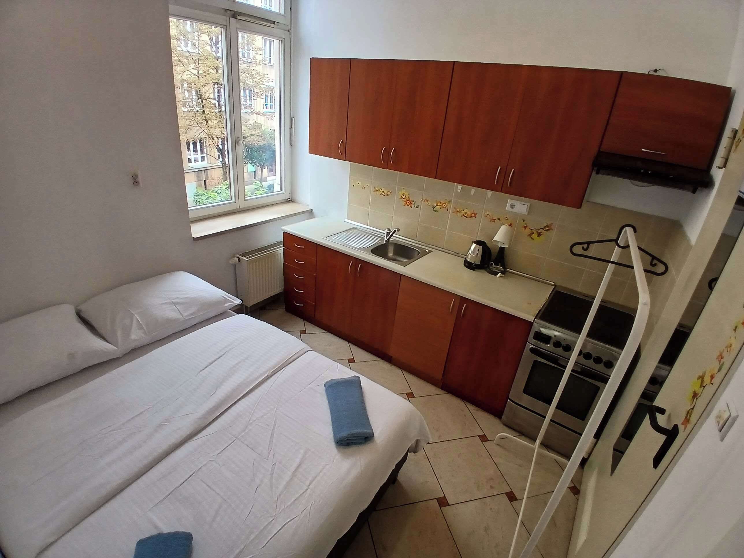 A small, compact room with a bed, a kitchenette, and a window.