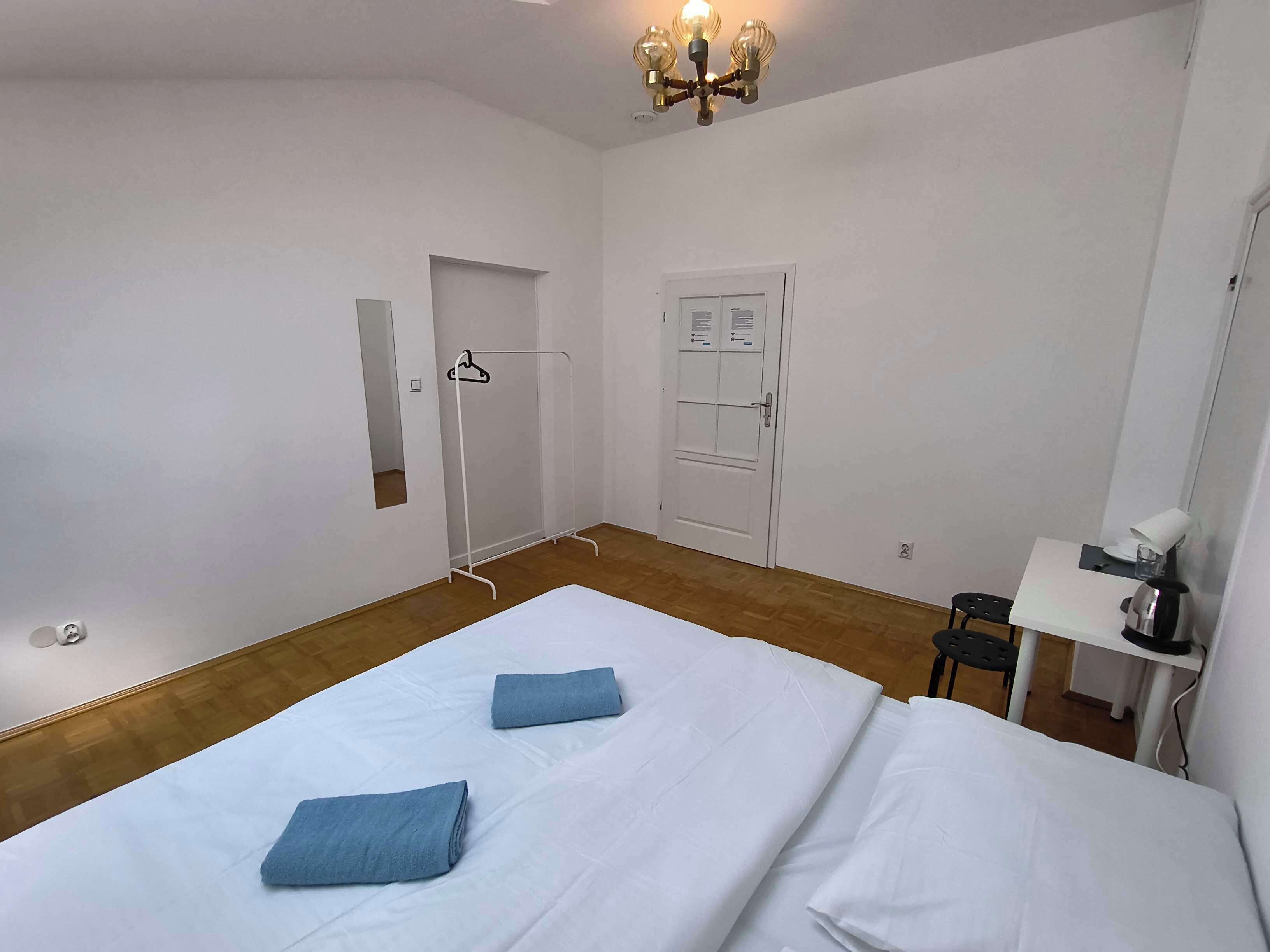 A hotel room with two beds, a desk, a chair, a wardrobe, and a chandelier.