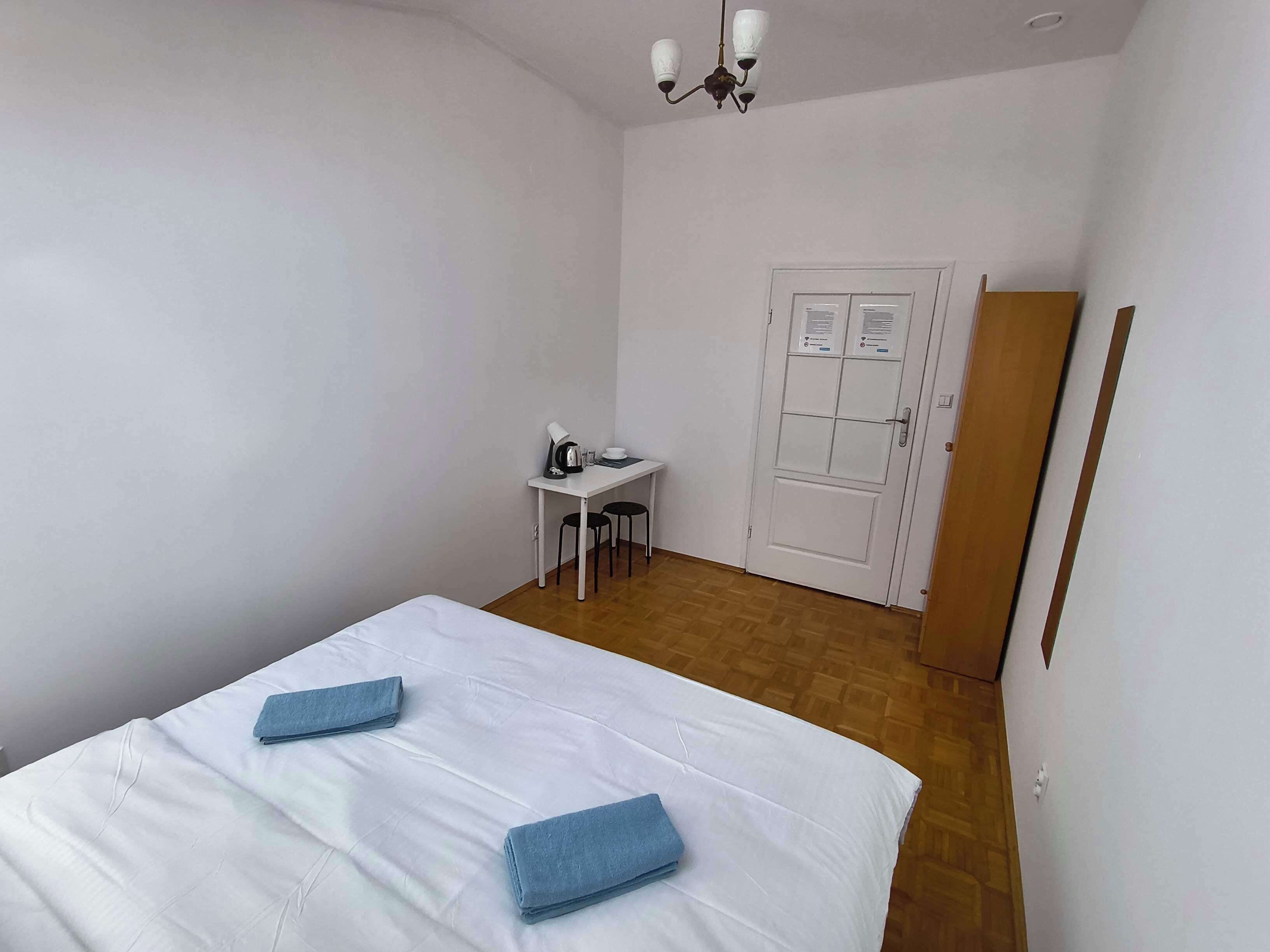 A hotel room with a bed, a desk, a chair, a door, and a light fixture.