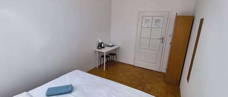 A hotel room with a bed, a desk, a chair, a door, and a light fixture.