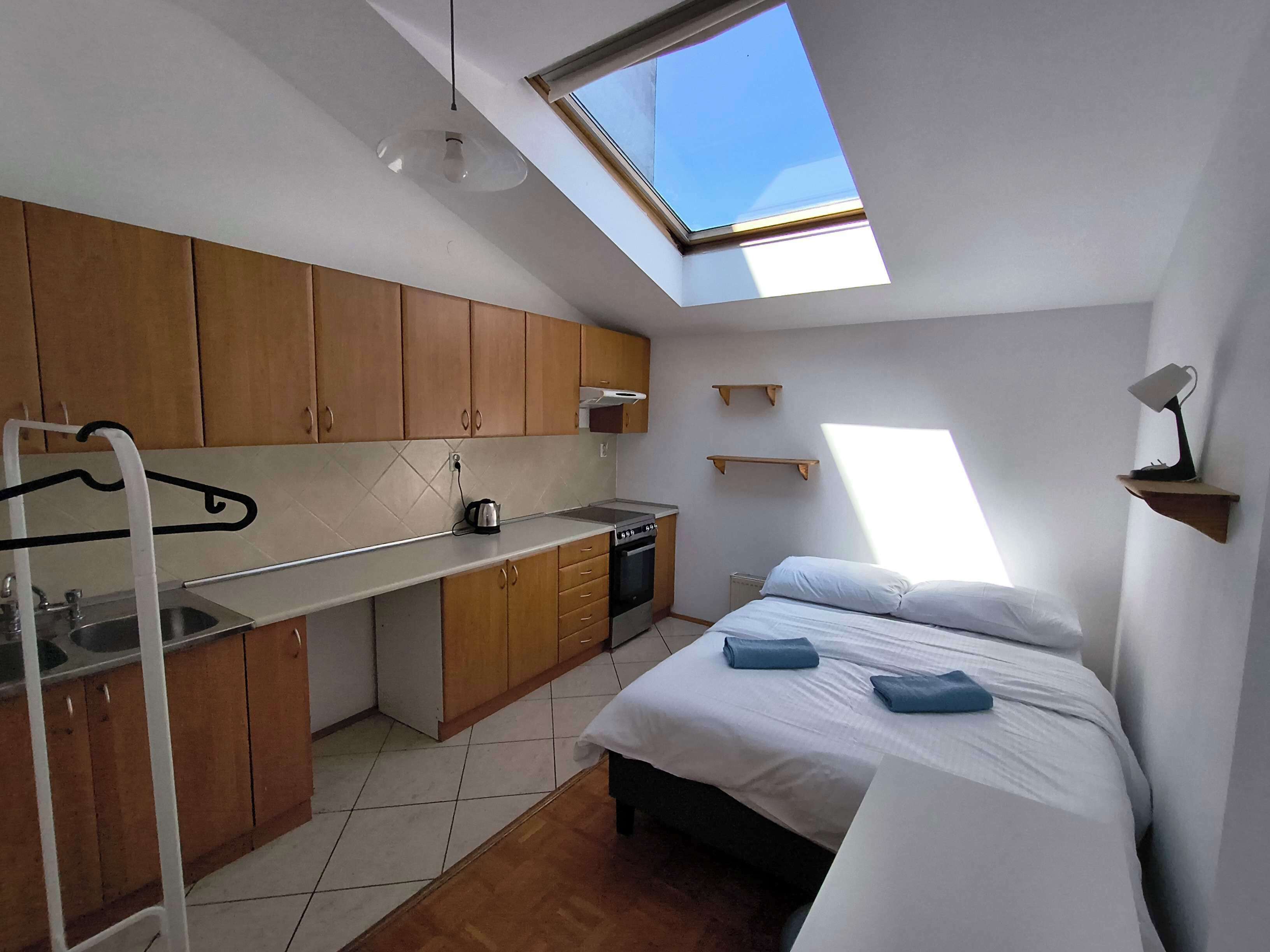 A compact room with a skylight, kitchenette, and a bed.