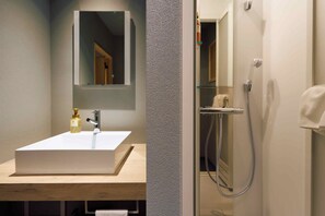 Un baño con un lavamanos blanco, un espejo encima y una zona de ducha con una toalla colgada en la pared.