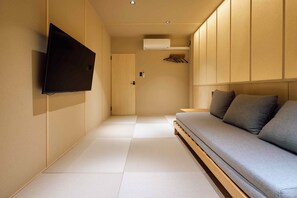 Ein schlicht eingerichteter Raum mit Tatami-Boden, einer Couch, einem Fernseher und einem Kleiderschrank.
