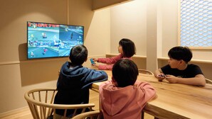 A group of children playing a racing game on a television screen in a room with wooden furniture. - Imakusa-so, Osaka, Tempozan - Tall Lantern - (大阪府大阪市港区築港3丁目)
