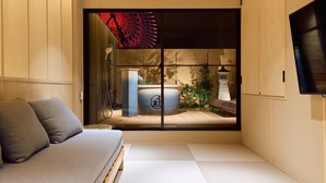 A minimalist room with tatami flooring, a low wooden bed, a grey sofa, and a sliding shoji screen with a red decorative element. - Imakusa-so, Osaka, Tempozan - Tall Lantern - (大阪府大阪市港区築港3丁目)