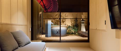 A minimalist room with tatami flooring, a low wooden bed, a grey sofa, and a sliding shoji screen with a red decorative element.