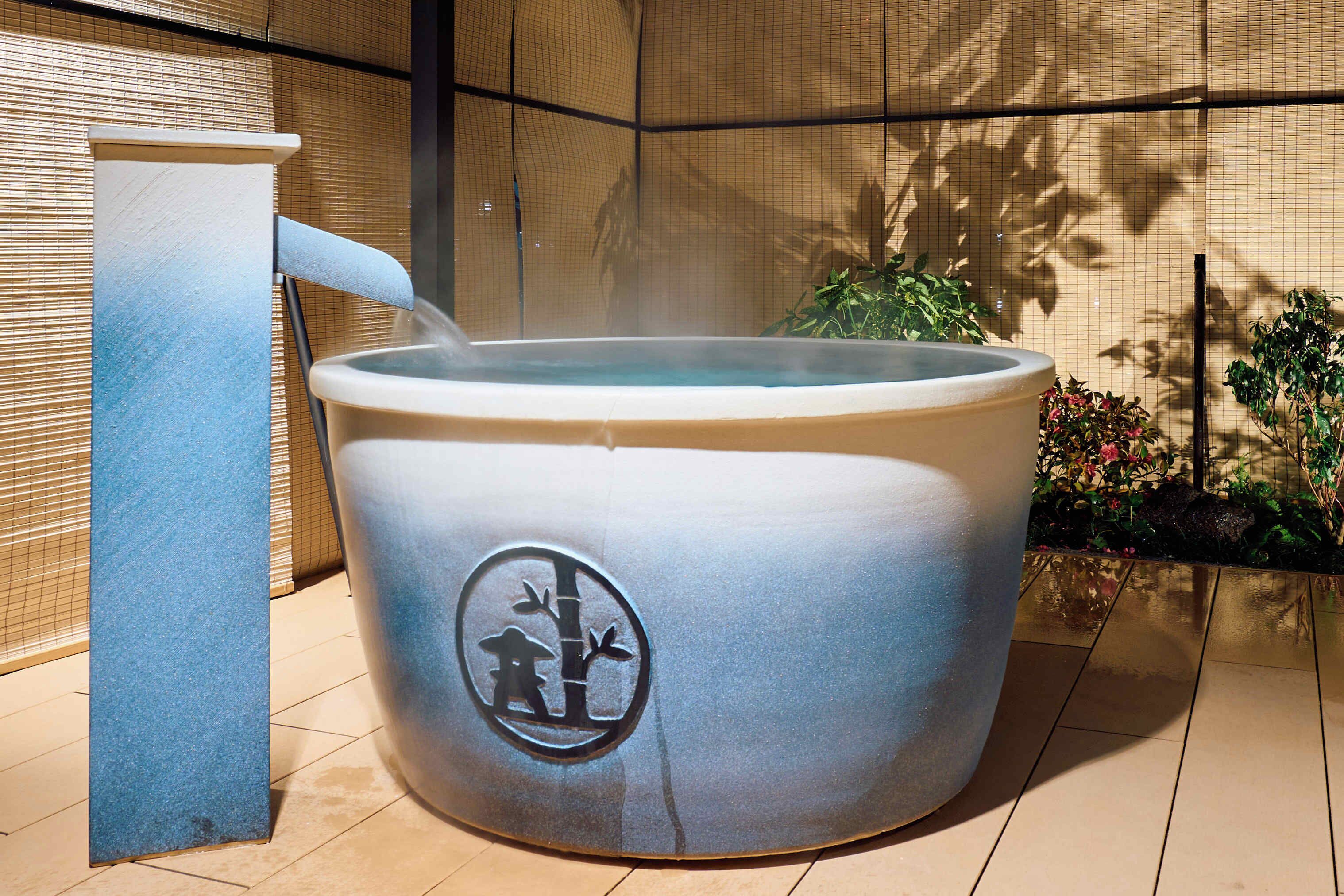 A hot tub with a logo, a stone structure, and a bamboo fence in the background.