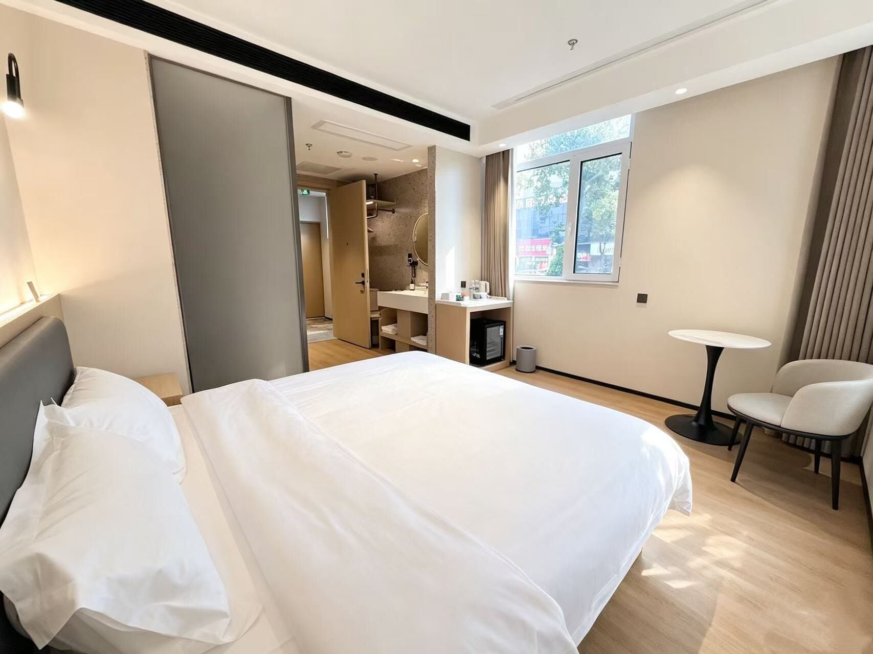 A hotel room with a large bed, a desk, a chair, a small table, and a window.